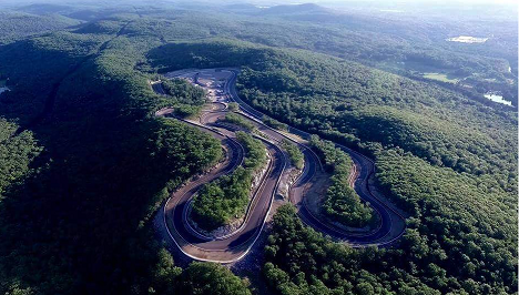 Summer aerial view of the full circuit looping through dense green forest on a mountaintop.