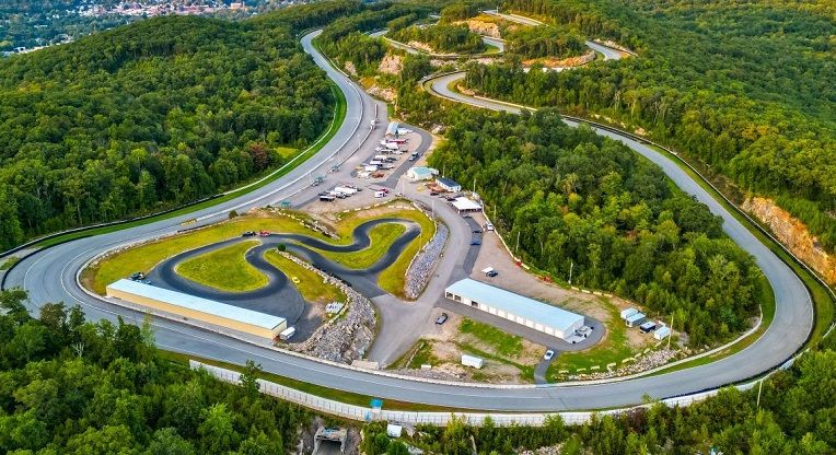 Aerial view of the paddock and infield: garages, parked trailers and a small infield circuit, bordered by the main track.